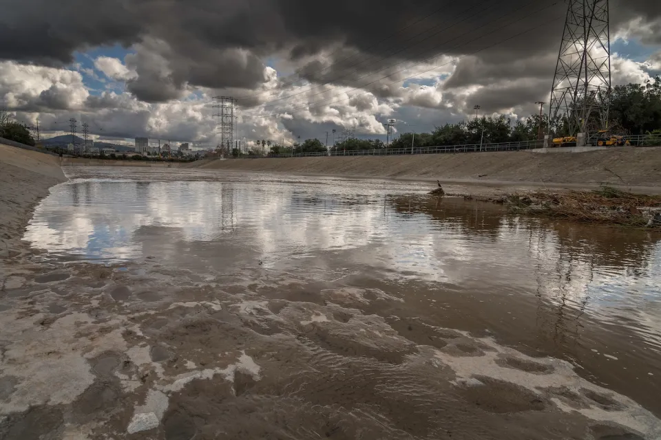 Low view of Glendale Narrows section of Los Angeles River with concrete bottom and cloudy storm sky over head.